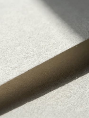 Macro detail of heavy textured cotton paper under sharp directional sunlight, casting deep geometric shadows.