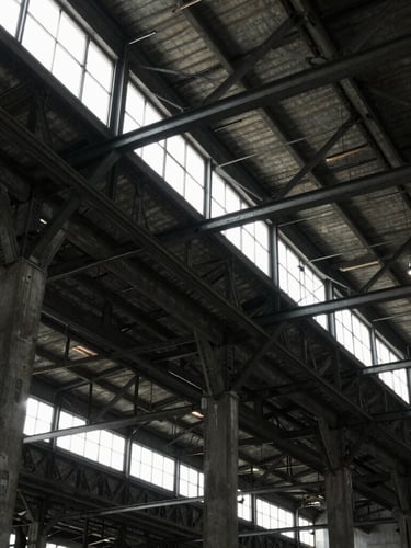 Architectural detail of an industrial warehouse ceiling, exposed steel trusses and concrete pillars, moody natural light from high clerestory windows.