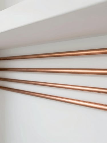 Architectural wide shot of a pristine home utility room, perfectly aligned parallel copper water lines with bright bronze fittings against a clean white wall, illuminated by soft natural side light.