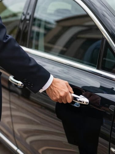 Close-up of a professional chauffeur in a dark suit opening the door of a spotless black executive sedan, bright natural Mediterranean daylight, sharp focus on the chrome handle