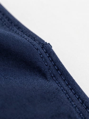 Macro close-up of heavy cotton fabric texture, raw stitching details on a navy blue pocket seam, soft natural overcast daylight, high detail.