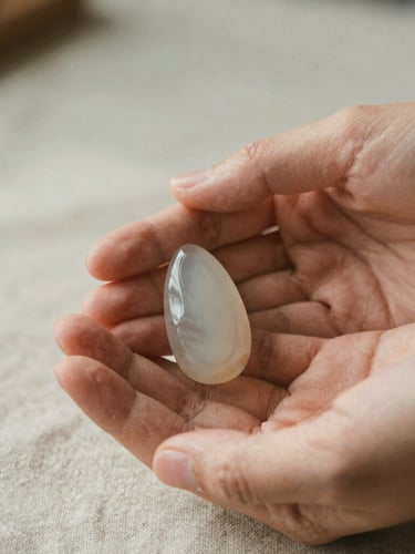 A close-up of hands gently holding a single raw chalcedony bead, soft morning light washing over warm linen textures, shallow depth of field, 35mm film.