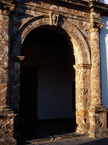 Imposing traditional stone archway of historic Spanish colonial architecture in Nochistlán, Zacatecas, warm golden-hour side lighting, deep shadows, rich architectural textures, 35mm film.