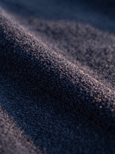 Macro close-up of heavy-weight cotton fleece stitching, natural golden-hour side light, rich deep navy fabric texture, shallow depth of field, 35mm
