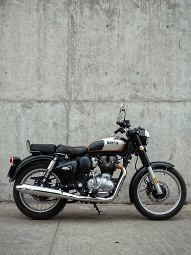 Wide three-quarter view of a Royal Enfield Classic 350 parked against a bare concrete wall in diffused north-facing daylight, frame geometry and chrome exhaust pipe fully visible, no rider present