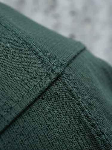 Macro close-up of dark forest green technical fabric weave, sharp focus on clean seams and breathable structure under cool overcast daylight