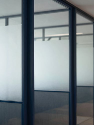 Portrait crop of a clean, modern financial office interior, focus on architectural glass partitions, soft natural daylight, deep navy and slate tones.