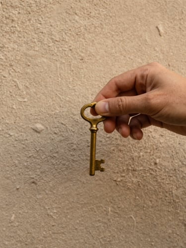 Close-up of a hand holding an old brass key against a textured plaster wall, soft morning light, warm earthy tones
