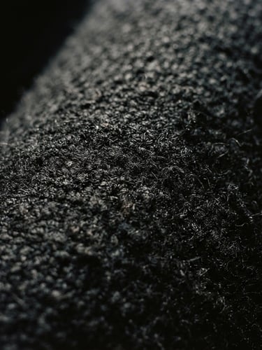 Extreme close-up of heavy black wool fabric texture, deep shadows, harsh side lighting, minimalist editorial photography, 35mm grain