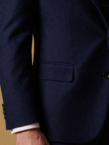 High-fashion editorial crop of a man in a sharp navy blue wool suit, dramatic side lighting, rich fabric texture visible, gold cufflink detail.