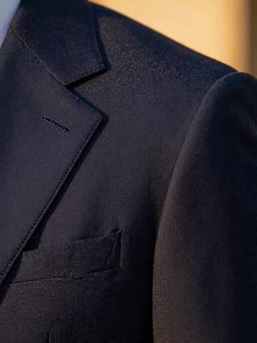 Macro close-up of a sharp navy suit shoulder, golden-hour side lighting highlighting the fine fabric weave and hand-stitched lapel, luxurious editorial fashion photography
