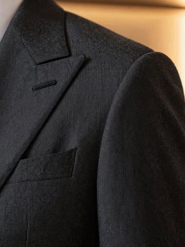 Close-up of a meticulously tailored charcoal grey suit shoulder and lapel, showcasing the intricate fabric weave, soft shoulder pad structure, warm side window light.