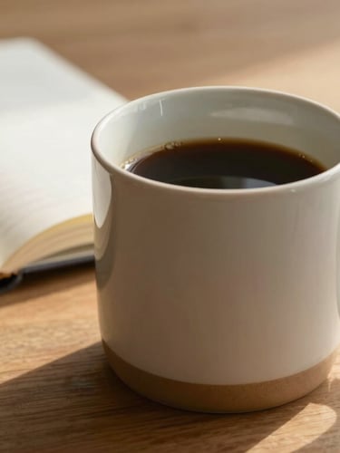 A ceramic mug resting on a wooden table next to an open notebook, soft morning light, warm sand tones.