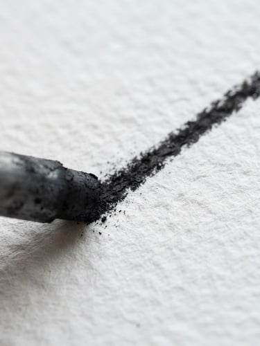 Macro photograph of a charcoal stick drawing a crisp, dark line on heavily textured white watercolor paper, bright natural studio daylight, sharp focus, high-detail texture