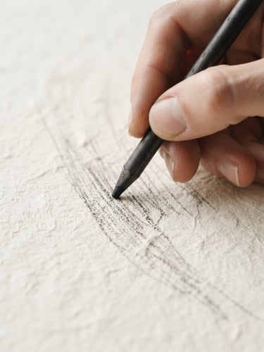 Macro shot of a hand holding a charcoal stick, drawing fine lines on heavily textured cream paper, bright natural north daylight, sharp focus, 35mm
