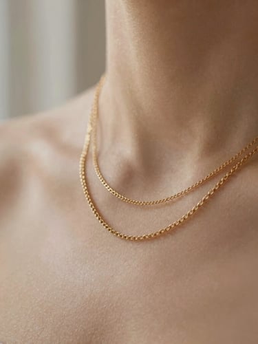 Macro close-up of layered 14k gold-filled necklaces on warm skin tone, soft natural window light, sandy neutral background, 35mm