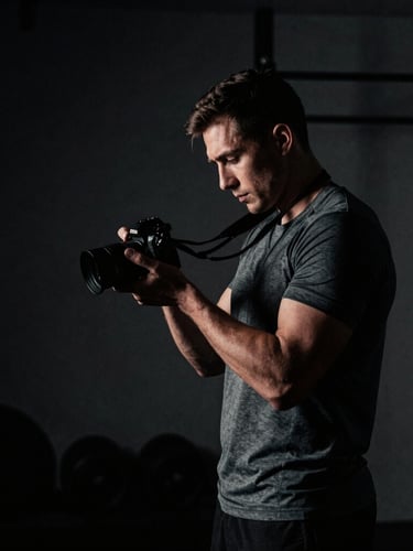 Dramatic side-lit portrait of a professional male athlete reviewing content on a camera in a dark, brutalist gym, high contrast, desaturated tones, 35mm film grain.