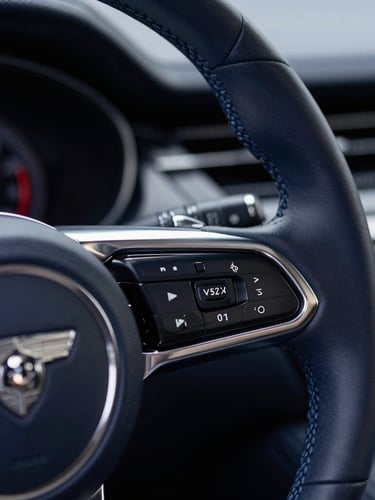 Close-up of a luxury car steering wheel, leather stitching and polished metallic details, soft studio lighting, deep navy tones, sharp focus, 50mm