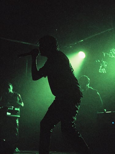 Gritty concert photography with low-key stage lighting, high-contrast neon green backlights, artist in motion on stage, 35mm film style