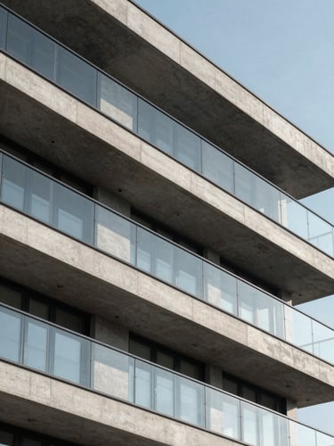 Sharp architectural close-up of a modern concrete and glass residential facade, clean angles, crisp daylight, high-contrast shadows
