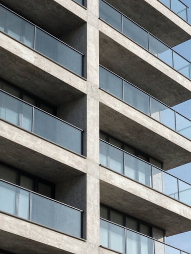 Sharp architectural close-up of a modern concrete and glass residential building, clean geometric lines, bright daylight, high contrast, minimalist composition.