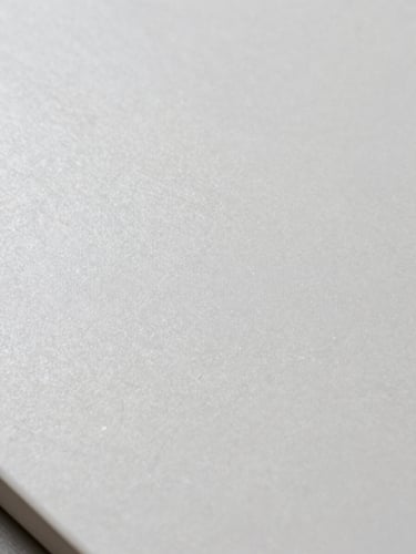 Extreme close-up of large-format porcelain tile surface under north-facing studio light, revealing fine crystalline texture and matte finish, cool white tones, sharp material detail, no human elements
