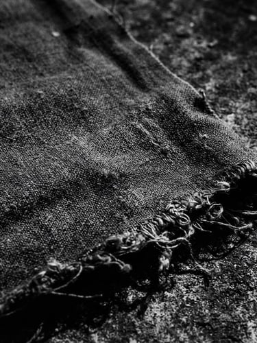 moody monochrome photography of a heavy cotton fabric texture with raw edges, harsh shadows, concrete background, 35mm film style