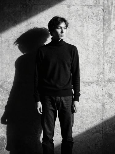 Moody monochrome shot of a model standing in a contemplative pose against a raw concrete wall, harsh shadows, 35mm film