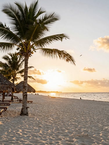 Tropical beach sunset with palm trees, thatched umbrellas, and lounge chairs on white sand.