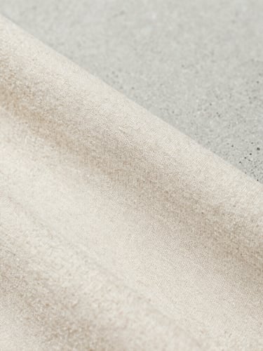 Close-up macro shot of the weave of a high-grammage organic cotton fabric, showing fine texture and natural fibers, under soft natural daylight, minimalist editorial product photography, sharp focus, neutral concrete background, 35mm
