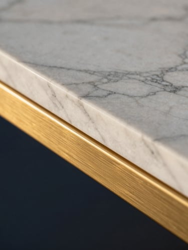Tight abstract shot of premium architectural materials, white Arabescato marble meeting brushed brass trim, dramatic side lighting