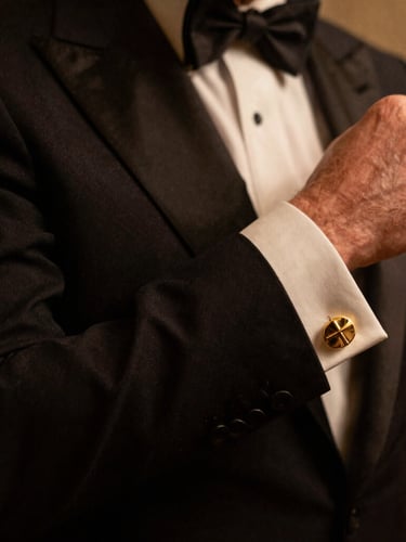 Close-up of a perfectly tailored bespoke tuxedo sleeve and gold cufflink, warm low-key atmospheric lighting, deep shadows, luxury Mayfair aesthetic