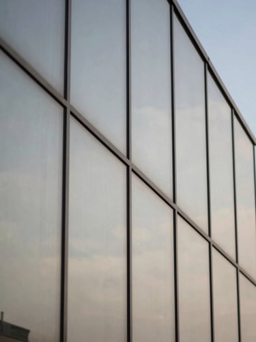 Macro shot of architectural glass panels reflecting neutral daylight and a crisp blue sky.