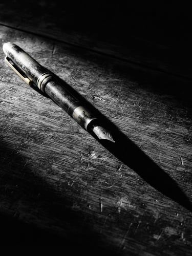 Stark high-contrast black and white photography of a single heavy vintage pen casting a long, sharp shadow on a dark textured desk, harsh single-source spotlight, deep chiaroscuro, 35mm film grain