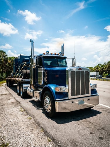 Low-angle heroic shot of a clean, heavy-duty semi-truck parked on a Florida highway shoulder under bright midday sun, cargo straps visible, wide-angle lens, 35mm, high-contrast saturated tones.