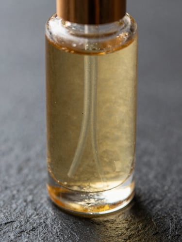 Extreme close-up of a glass beauty serum bottle on dark stone surface, golden liquid catching soft atelier light, fine texture of the stone visible, no model or face