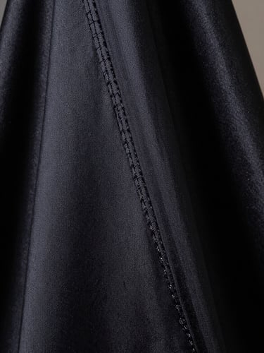 Extreme close-up of draped dark silk couture fabric, precise architectural seam running diagonally, soft directional atelier light from the left, no human face