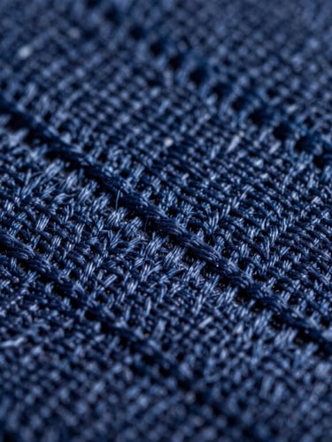 Extreme macro close-up of high-density navy blue embroidery stitches on heavy-duty canvas fabric, showing precise thread alignment and physical relief under sharp studio lighting.
