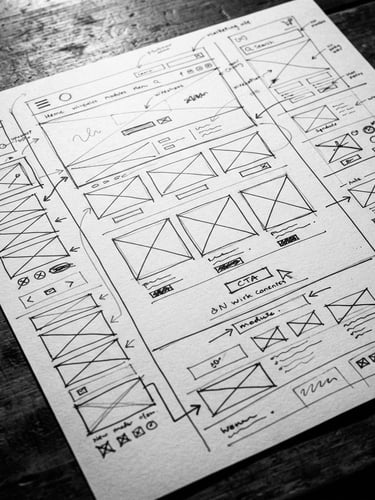 Tight macro shot of an annotated marketing wireframe on a desk with sharp direct studio shadows, high-contrast, black and white