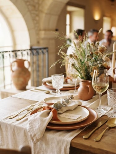 Sunlit interior view of a beautifully set table for a small celebration, warm neutral tones, soft focus on elegant place settings, architectural details of the venue visible in background, natural window light.