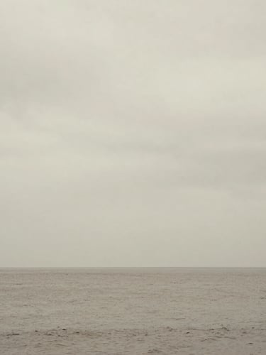 Calm sea under a heavy overcast sky, horizon line barely visible, minimalist fine art photography, desaturated earth tones