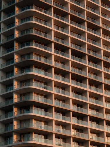 Tight architectural detail of a luxury Miami high-rise building at dusk, warm light glowing from within, clean geometric lines.