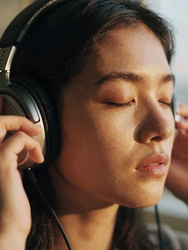 Close-up of a person listening to headphones with closed eyes, soft golden-hour light illuminating their face, rich emotional tones, shallow depth of field, 35mm film grain