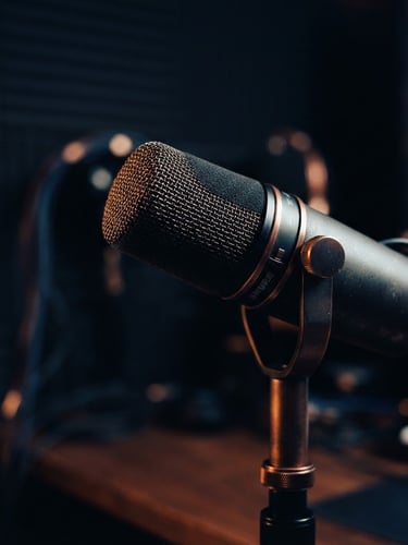 High-quality studio microphone, close-up, moody directional studio lighting, warm highlights, shallow depth of field, 35mm, deep navy and copper tones, off-center to the right.