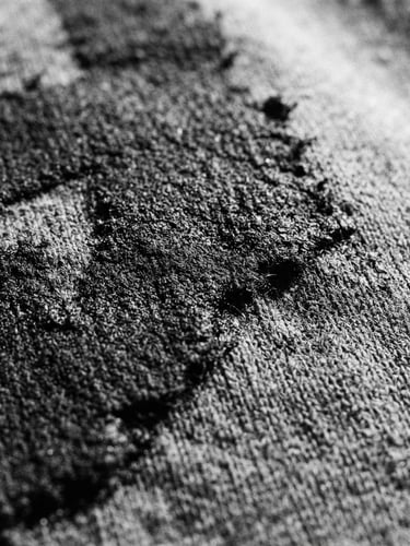 Extreme close-up of raw black ink texture on heavy grey cotton fabric, harsh direct sunlight casting sharp shadows, 35mm film grain