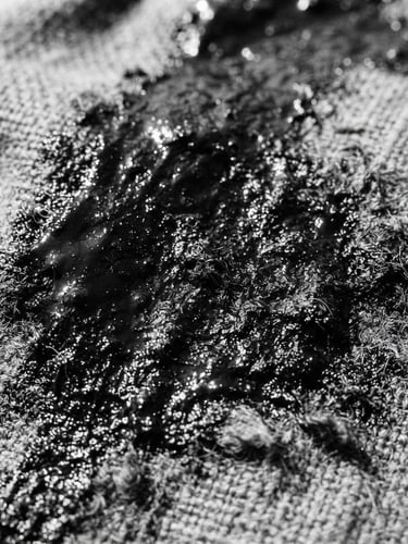 Extreme close-up of thick wet black ink texture on raw heavyweight grey cotton fabric, harsh direct sunlight, high-contrast, 35mm film grain