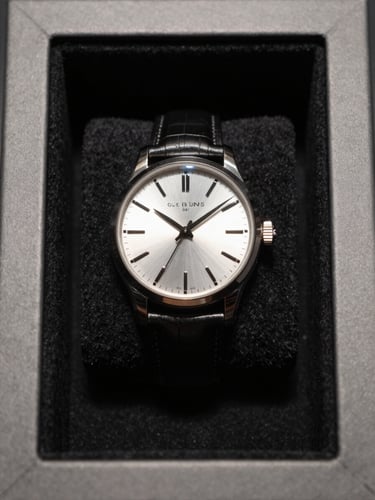 Overhead study of a luxury watch resting on a black velvet surface inside a minimal display vault, single controlled north-facing light source grazing the dial to reveal every brushed and polished surface facet, deep shadow at frame edges, no hands or faces