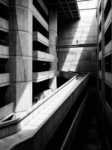 Stark monochrome photograph of a brutalist concrete atrium, sharp directional light casting deep diagonal shadows, clean architectural lines, minimalist composition.