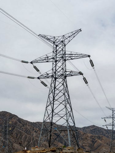 Low-angle heroic shot of high-voltage transmission towers stretching into Utah mountain backdrop, cold overcast daylight, desaturated steel tones with sharp blue accents