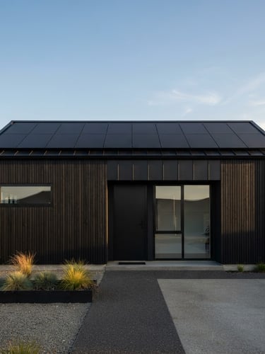 Straight-on architectural elevation of a modern black-clad minimalist house at golden hour, matte-black solar panels integrated flush into the roofline, negative space, sharp focus